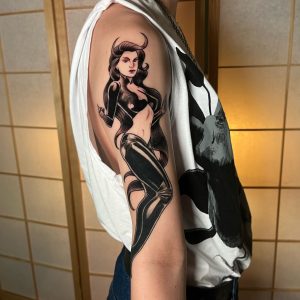 Nahaufnahme eines schwarzen Oberarm-Tattoos mit Fantasy-Figur, feinen Linien und Schattierungen.