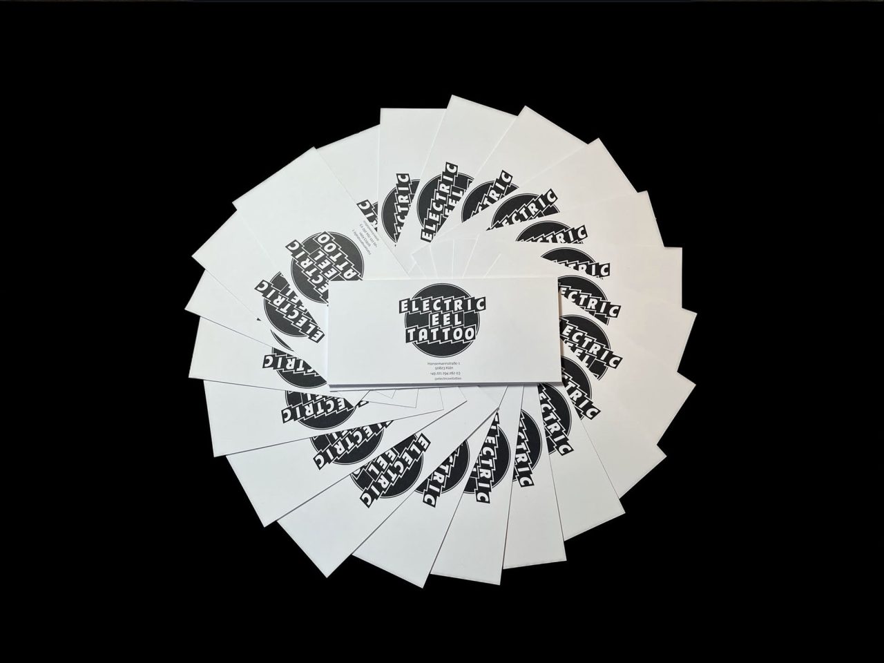 Fotografie von Electric Eel Tattoo Gutscheinen mit Studio-Logo und Kontaktdaten auf schwarzem Hintergrund.