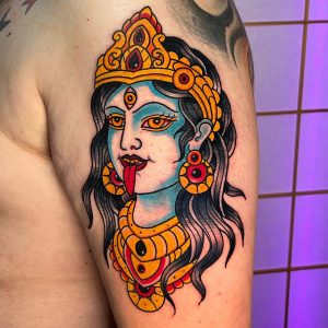 Nahaufnahme eines farbigen Oberarm-Tattoos mit Kali-Motiv, kräftigen Konturen, Schmuckelementen und leuchtenden Farben.